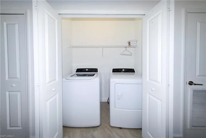 Washroom with washing machine and dryer and light tile patterned flooring