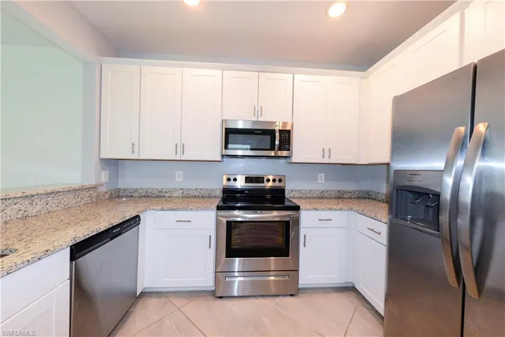 Kitchen featuring stainless steel appliances, white cabinetry, light stone countertops, light tile patterned flooring, and recessed lighting