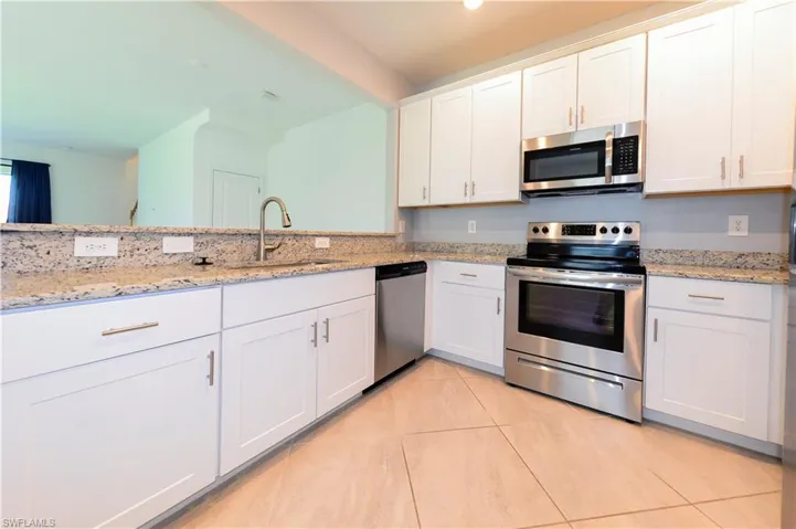 Kitchen featuring stainless steel appliances, white cabinetry, light tile patterned floors, and light stone counters