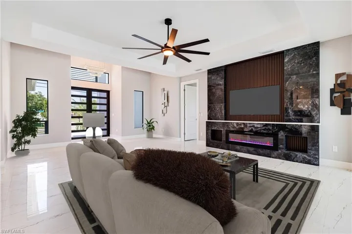 Living area featuring a tray ceiling, marble tiled floors, baseboards, a ceiling fan, and a premium fireplace