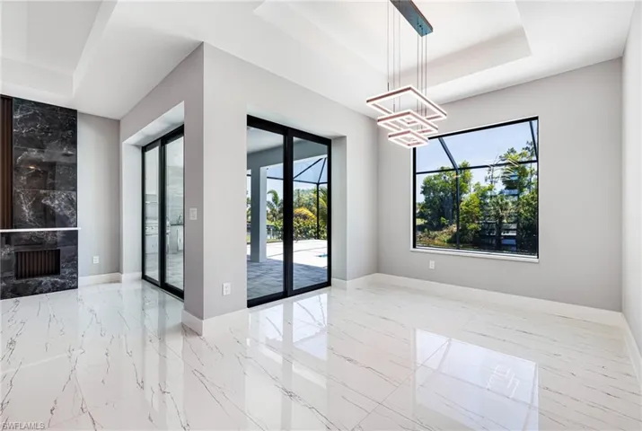 Empty room featuring a tray ceiling, plenty of natural light, a chandelier, and marble tiled flooring