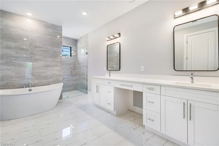Full bathroom with marble look tiles, a stall shower, double vanity, a soaking tub, and recessed lighting