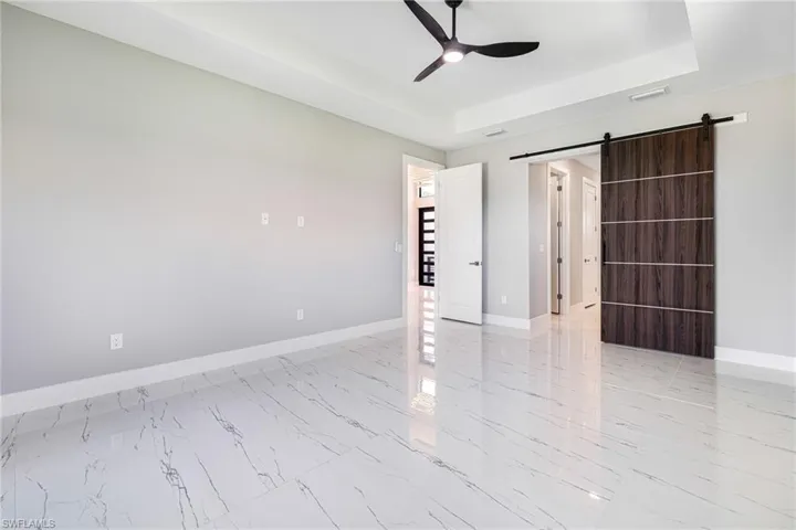 Unfurnished room with a ceiling fan, a barn door, a tray ceiling, and baseboards