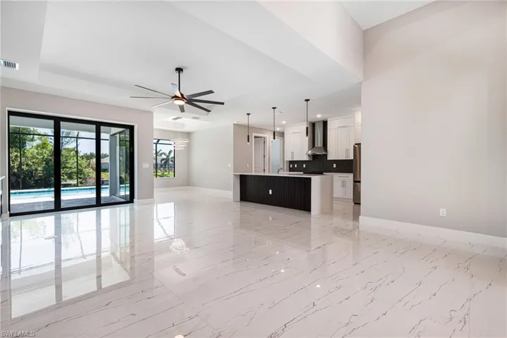 Unfurnished living room featuring baseboards, a raised ceiling, a ceiling fan, light marble finish flooring, and recessed lighting