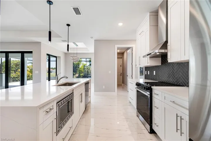 Kitchen with stainless steel appliances, baseboards, a sink, tasteful backsplash, and wall chimney range hood