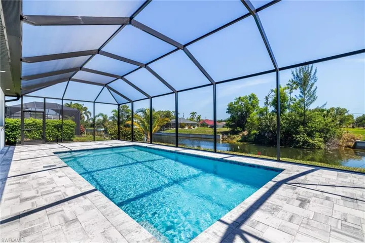 Outdoor pool with a water view, a patio area, and glass enclosure