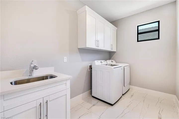 Washroom featuring cabinet space, washer and dryer, light marble finish flooring, and baseboards