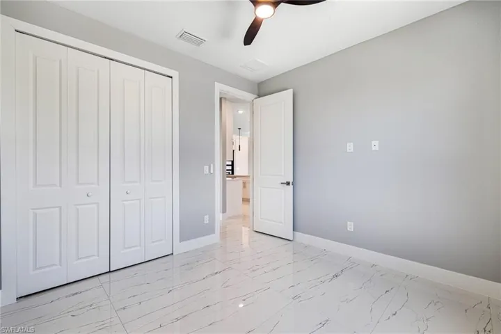Unfurnished bedroom featuring baseboards, a closet, light marble finish flooring, and ceiling fan