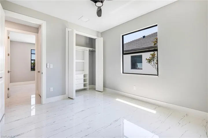 Unfurnished bedroom featuring marble finish floors, baseboards, a closet, and a ceiling fan