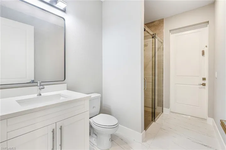 Full bath with marble finish flooring, a shower stall, vanity, toilet, and baseboards
