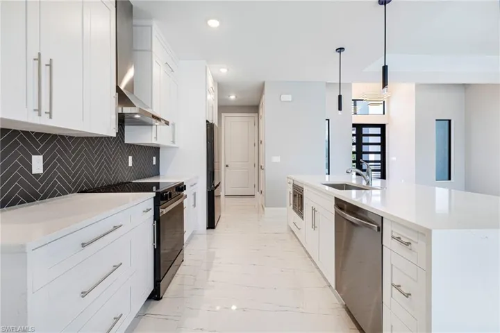 Kitchen featuring stainless steel appliances, light marble finish floors, wall chimney range hood, a sink, and backsplash