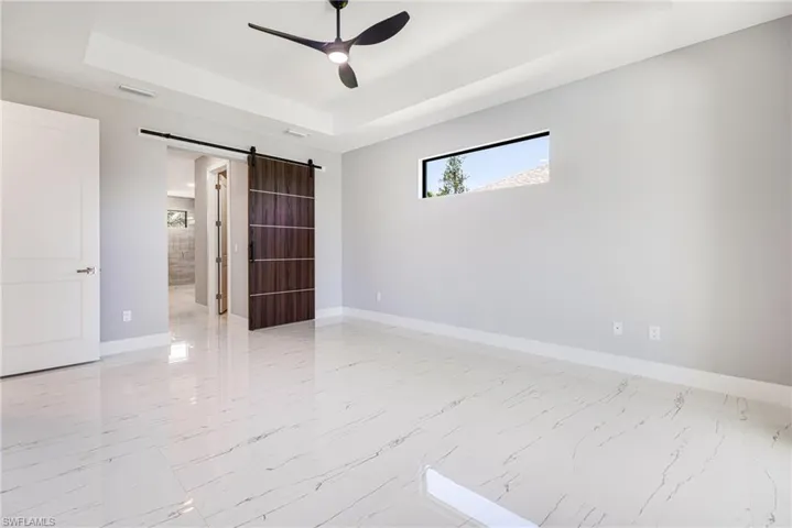 Spare room with a barn door, a tray ceiling, baseboards, and ceiling fan
