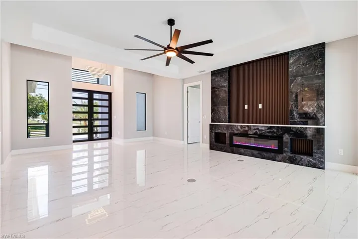 Unfurnished living room with a raised ceiling, baseboards, ceiling fan, and marble tiled floors