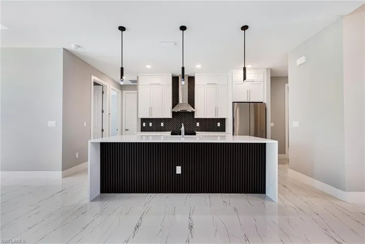 Kitchen with wall chimney range hood, freestanding refrigerator, light marble finish flooring, white cabinetry, and recessed lighting