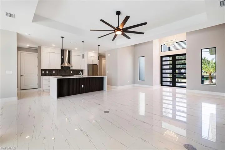 Kitchen featuring freestanding refrigerator, wall chimney range hood, a tray ceiling, open floor plan, and a center island with sink