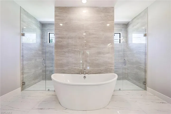 Full bath featuring baseboards, marble finish floors, a freestanding bath, and a stall shower