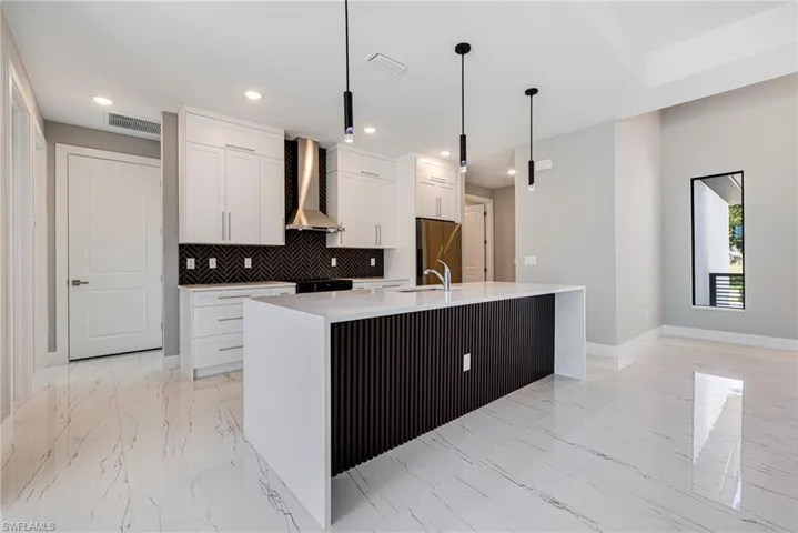 Kitchen featuring wall chimney range hood, baseboards, light marble finish flooring, tasteful backsplash, and recessed lighting