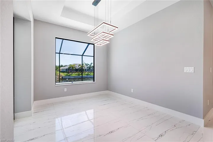 Empty room featuring marble finish flooring, a chandelier, baseboards, and a raised ceiling