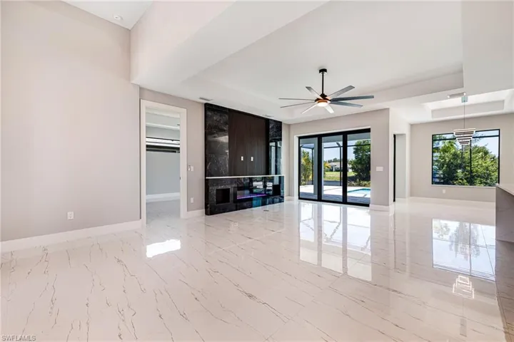 Unfurnished living room with a tray ceiling, baseboards, light marble finish flooring, and ceiling fan