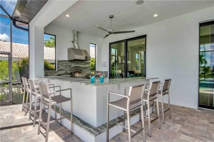 View of patio featuring exterior kitchen, a sunroom, glass enclosure, and a ceiling fan