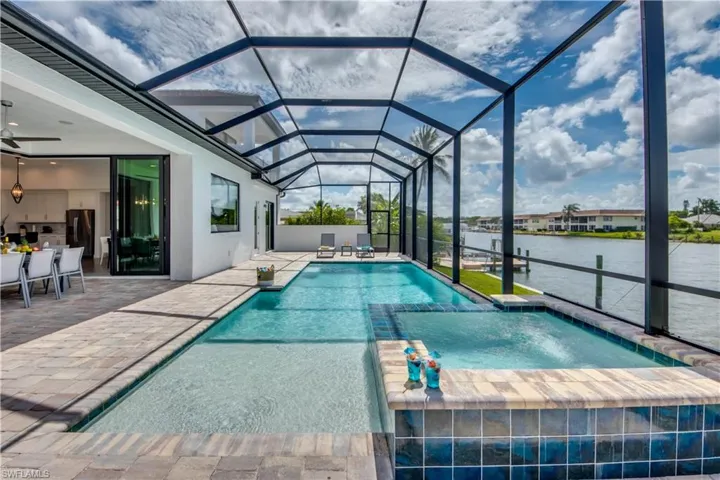 View of pool with a pool with connected hot tub, a water view, a sunroom, a patio area, and glass enclosure