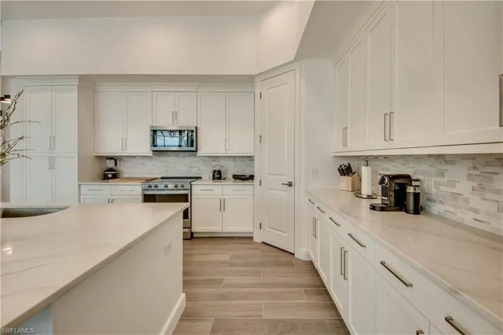Kitchen with appliances with stainless steel finishes, light stone counters, white cabinetry, wood finish floors, and decorative backsplash