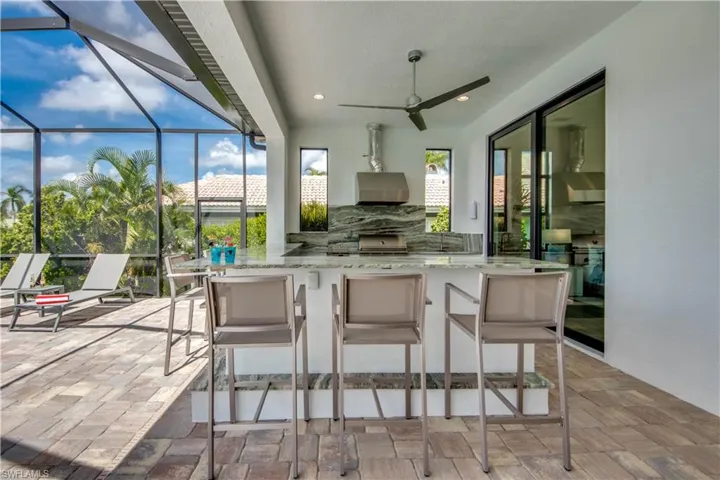 View of patio featuring exterior kitchen, a sunroom, glass enclosure, and a ceiling fan