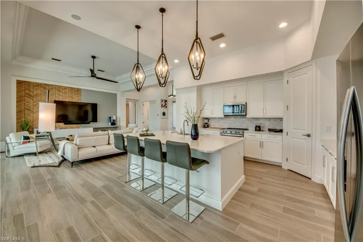 Kitchen with a kitchen breakfast bar, stainless steel appliances, white cabinetry, wood finish floors, and a kitchen island with sink