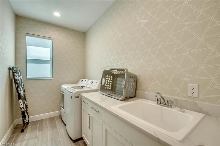 Washroom with washing machine and dryer, wood tiled floors, cabinet space, wallpapered walls, and recessed lighting
