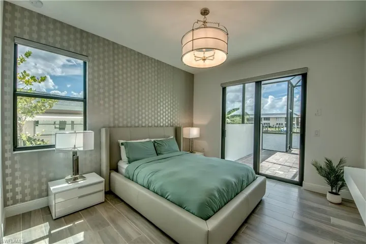 Bedroom with wallpapered walls, an accent wall, wood finish floors, a water view, and access to outside