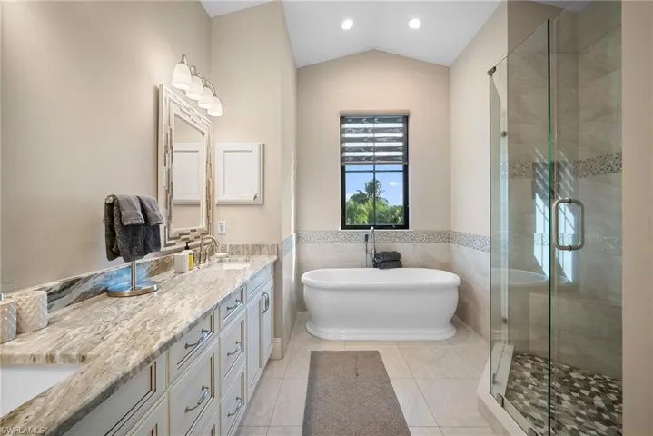 Bathroom featuring a freestanding tub, a stall shower, tile walls, double vanity, and light tile patterned floors