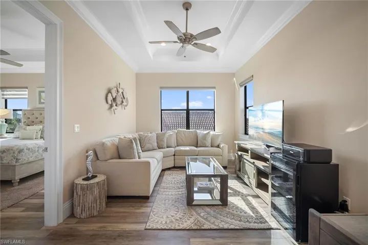 Den featuring ornamental molding, a tray ceiling, wood finished floors, and a ceiling fan