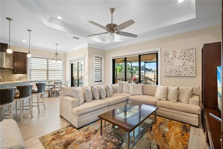 Living room with light wood-style flooring, crown molding, a tray ceiling, recessed lighting, and a chandelier