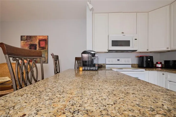Kitchen featuring white cabinets, a breakfast bar, granite counters, and white appliances