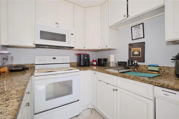 Kitchen featuring dark stone countertops, white cabinetry, and white appliances
