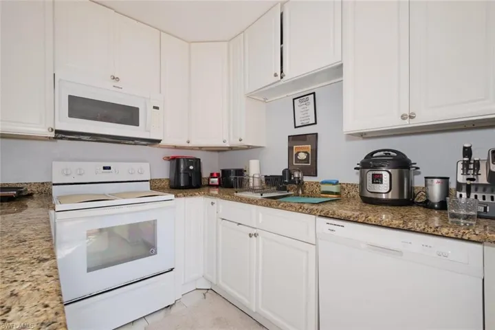 Kitchen with white cabinetry, dark stone countertops, and white appliances