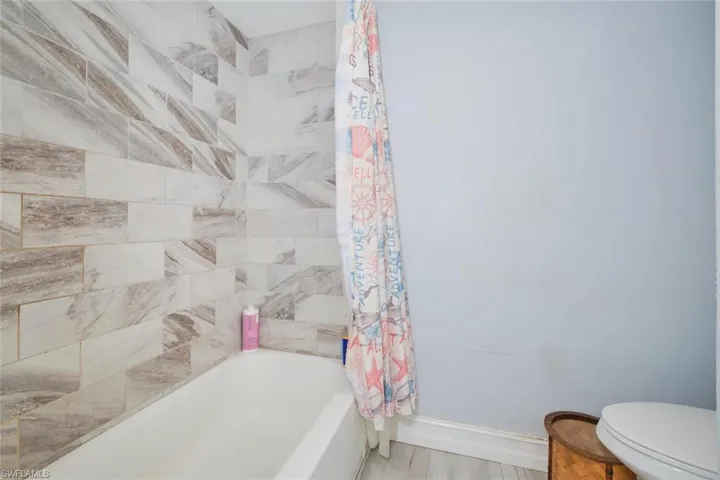 Bathroom with toilet, shower / bathtub combination with curtain, and hardwood / wood-style floors