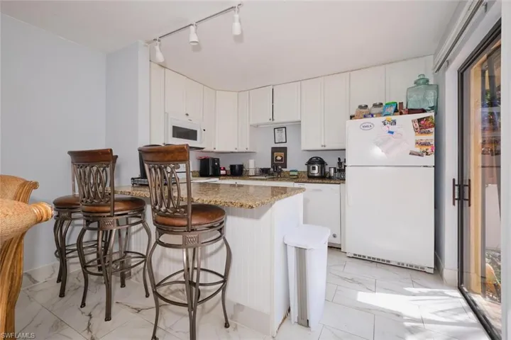 Kitchen featuring, granite counters, white cabinetry, white appliances, and light tile patterned floors