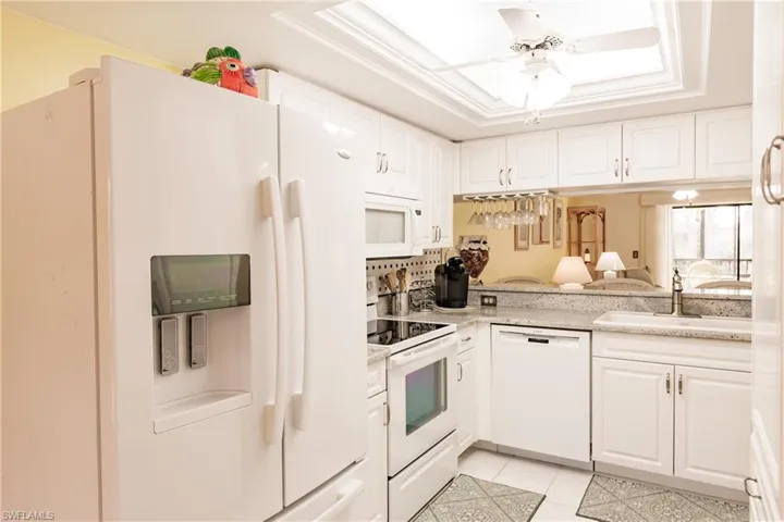 Kitchen featuring white appliances, white cabinetry, light stone counters, sink, and a tray ceiling