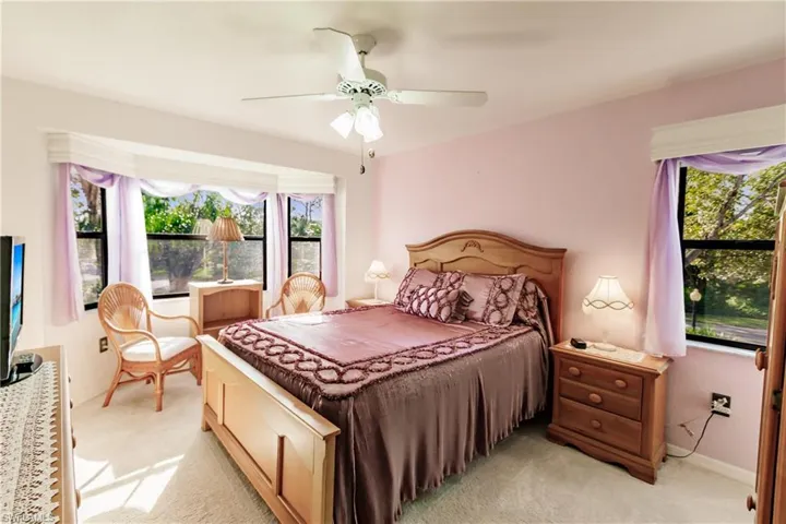 Bedroom featuring bay window with updated coverings, light colored carpet ceiling fan