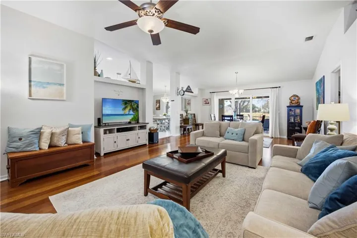 Living room featuring ceiling fan, wood finished floors, hanging lights, and vaulted ceiling