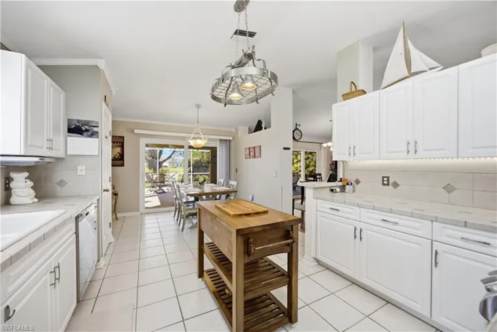 Kitchen with backsplash, white cabinets, crown molding, hanging light fixtures, and light tile patterned floors