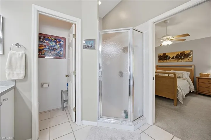 Ensuite bathroom with a shower stall, vanity, a ceiling fan, light tile patterned floors, and light colored carpet