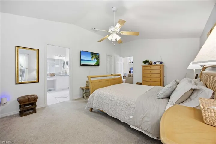 Carpeted bedroom with lofted ceiling, a ceiling fan, and ensuite bath
