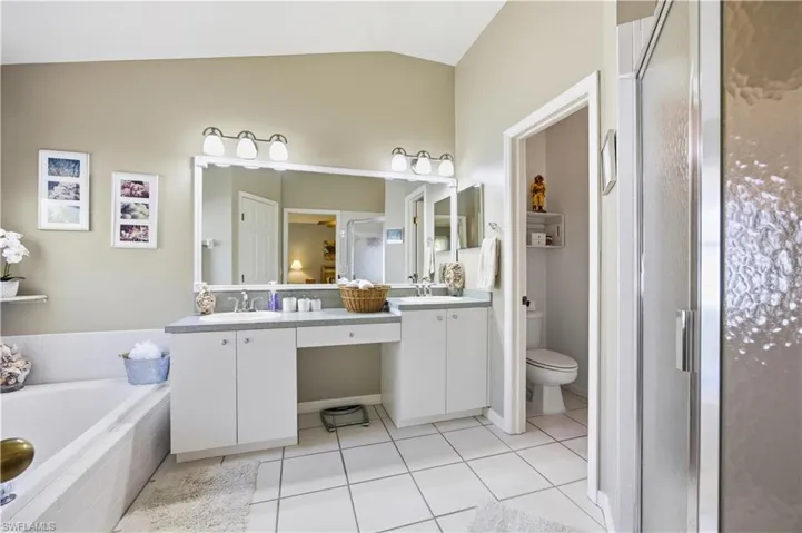 Full bath with double vanity, a stall shower, light tile patterned floors, a bath, and vaulted ceiling