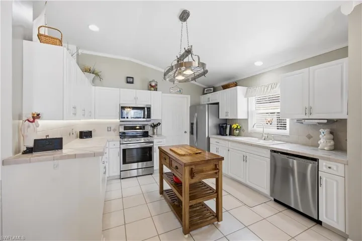 Kitchen with tasteful backsplash, stainless steel appliances, lofted ceiling, crown molding, and white cabinetry