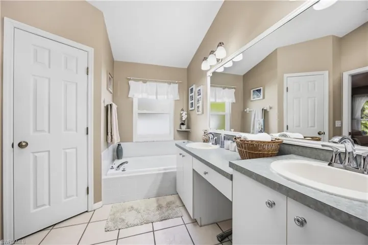 Full bath with double vanity, light tile patterned floors, and a bath