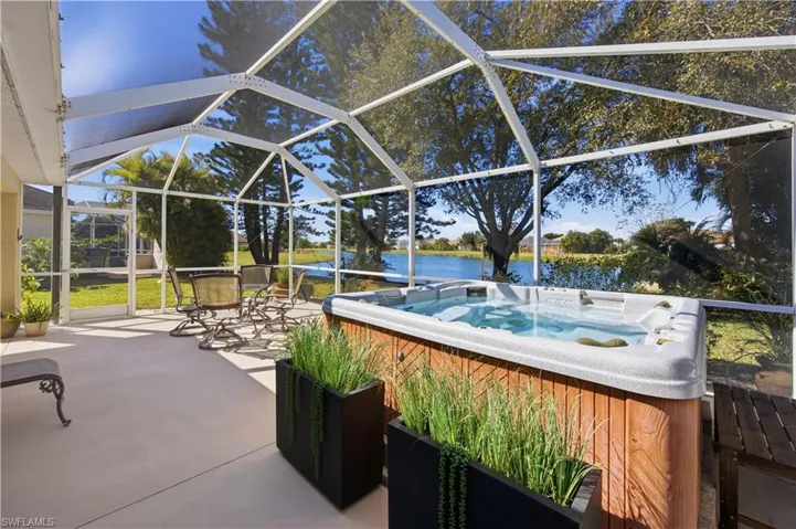 View of patio / terrace featuring glass enclosure, a sunroom, a water view, and a hot tub