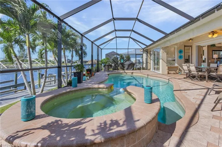 View of pool with a lanai, an in ground hot tub, a water view, and a patio