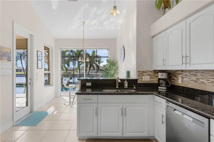 Kitchen featuring dark stone counters, sink, pendant lighting, a water view, and dishwasher
